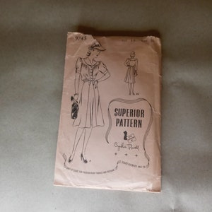 Op de afbeelding: Een vintage naaipatroon voor een jurk, met een vrouw die een jurk draagt met een kraag en een riem. Het patroon is gelabeld "Superior Pattern" en "Cynthia Powell". Het patroonnummer is 9743 en de maat is 18.