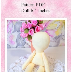 May include: A 6-inch doll pattern PDF. The doll is made of white fabric and is sitting on a white doily. The doll is surrounded by pink roses.