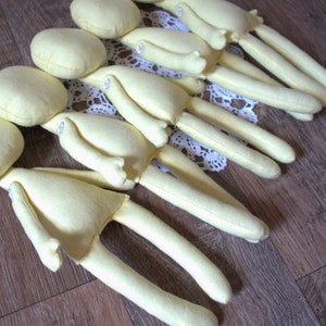 Blank dolls with long limbs and round heads. The dolls are arranged in a row on a light brown wooden surface.