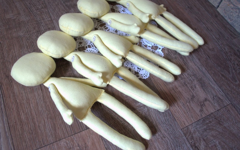 Blank dolls with long limbs and round heads. The dolls are arranged in a row on a light brown wooden surface.
