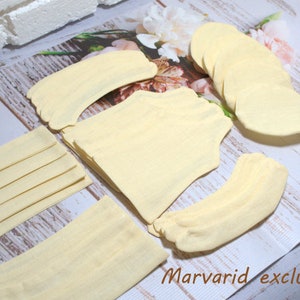 May include: A collection of light yellow socks and sock components arranged on a wooden surface. The components include several pairs of socks, sock cuffs, and other sock parts. The text "Marvarid exclusive" is visible in the bottom right corner.