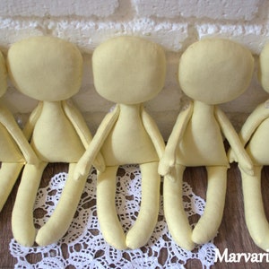 May include: Five unpainted yellow fabric doll bodies with limbs, sitting on a white lace doily.  The dolls are ready for customizing.