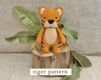 May include: A felt tiger toy with orange and brown stripes, standing on a wooden log. The toy has a beige belly and black eyes. The toy is surrounded by green felt leaves.