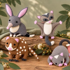 Può includere: Quattro figure di animali in feltro realizzate a mano, tra cui un bilby grigio con orecchie rosa, un quoll marrone maculato, un petaurista grigio con arti estesi e un piccolo opossum grigio con coda rosa, tutti con occhi a perla neri e dettagli cuciti.