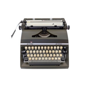 May include: A vintage olive green and black typewriter with off-white keys. The typewriter has the text "Scheidegger International" on the front. The keys are arranged in a QWERTY layout.