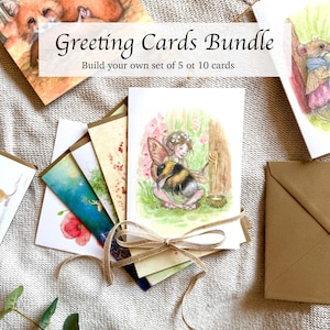 Op de afbeelding: Een bundel gevouwen wenskaarten samengebonden met een beige touwtje in een strik. De bovenste kaart toont een aquarelillustratie van een fee met een grote hommel en een honingdrupstok. De tekst op de afbeelding luidt Greeting Cards Bundle Build your own set of 5 ot 10 cards.