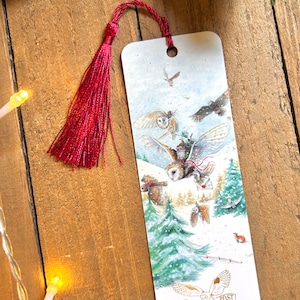 May include: A white bookmark featuring a winter scene with owls delivering letters. The owls are flying through a snowy forest with pine trees. The bookmark has a red tassel and the text "Owl Post" in gold lettering.