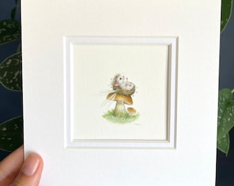 May include: A white fairy with wings sits on top of a mushroom with a brown cap and white stem. The fairy is holding a small pink flower in its hand. The mushroom is surrounded by green grass.
