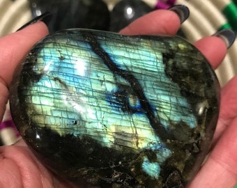May include: A heart-shaped labradorite crystal with a blue and green iridescent sheen. The crystal has a dark gray base with a natural, polished finish.