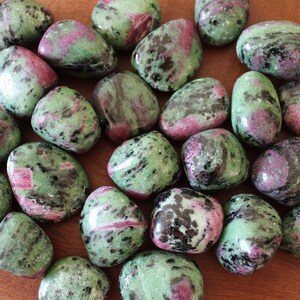 May include: A collection of green, pink, and black tumbled stones. The stones are smooth and polished, and they have a variety of patterns and colors.
