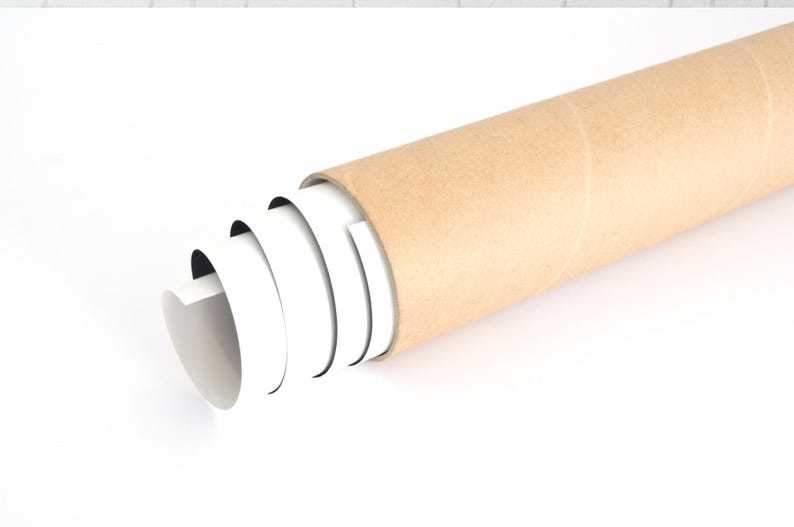 Puede incluir: Un rollo de impresi&oacute;n blanca emerge de un tubo de cart&oacute;n marr&oacute;n. El tubo cil&iacute;ndrico se encuentra en diagonal sobre una superficie blanca. La impresi&oacute;n blanca es parcialmente visible, lo que sugiere un p&oacute;ster o una obra de arte.