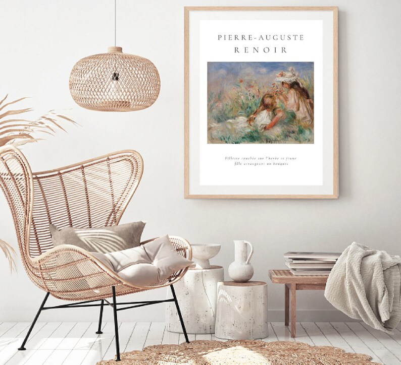 Puede incluir: Una impresi&oacute;n enmarcada de una pintura de Pierre-Auguste Renoir, que representa a dos figuras en un campo de flores. La impresi&oacute;n est&aacute; en un marco de madera clara, colgada en una pared blanca. La habitaci&oacute;n tambi&eacute;n incluye una silla de mimbre, una l&aacute;mpara colgante tejida y mesas auxiliares decorativas.