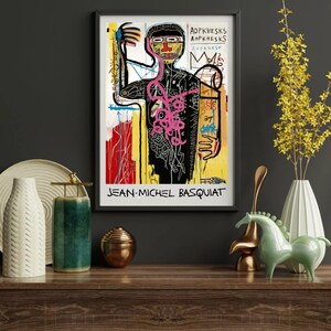Puede incluir: Impresi&oacute;n art&iacute;stica enmarcada que presenta una obra de arte de Jean-Michel Basquiat. La impresi&oacute;n muestra una figura negra con una estructura interna rosa, una corona y el nombre del artista. El fondo incluye trazos de pintura amarillos, rojos y blancos.