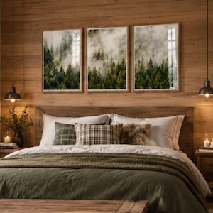 Peut inclure: Une chambre avec un lit doté d'une couette vert foncé, d'oreillers blancs et d'un coussin à carreaux. Au-dessus de la tête de lit en bois sont accrochés trois cadres représentant une forêt dense et brumeuse.