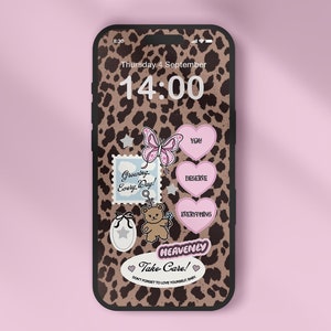 Peut inclure: Une coque de téléphone à imprimé léopard avec une horloge numérique affichant 14:00. La coque est décorée de plusieurs autocollants, dont un papillon, un ours en peluche et des cœurs avec les mots "You", "Deserve" et "Everything". Le texte "Heavenly Take Care!" est également présent sur la coque.