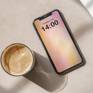 May include: A black smartphone with a blurred background on the screen displaying the time 14:00 and the date Thursday 4 July. A cup of coffee is in the foreground.