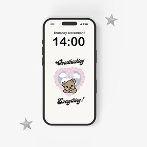 May include: A smartphone displaying a digital clock with the time 14:00 and the date Thursday, November 3. The background is a light pink with a cartoon bear in a heart-shaped frame. The text "Overthinking Everything!" is displayed below the bear.