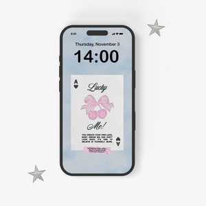 May include: A smartphone displaying a digital clock with the time 14:00 and the date Thursday, November 3. The phone screen also shows a digital image of an ace of spades playing card with a pink bow and cherries, and the text "Lucky Me! You create your own luck.  Baby, dream big and don't look back. It's time to believe in yourself more."