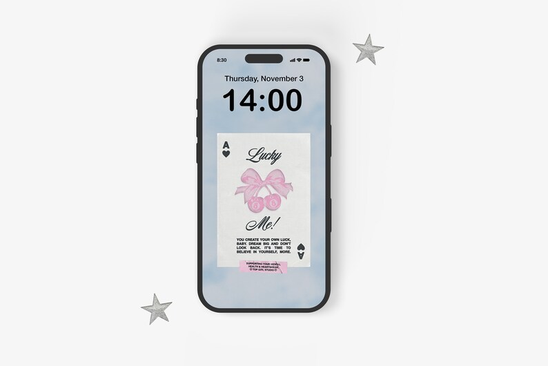 May include: A smartphone displaying a digital clock with the time 14:00 and the date Thursday, November 3. The phone screen also shows a digital image of an ace of spades playing card with a pink bow and cherries, and the text "Lucky Me! You create your own luck.  Baby, dream big and don't look back. It's time to believe in yourself more."