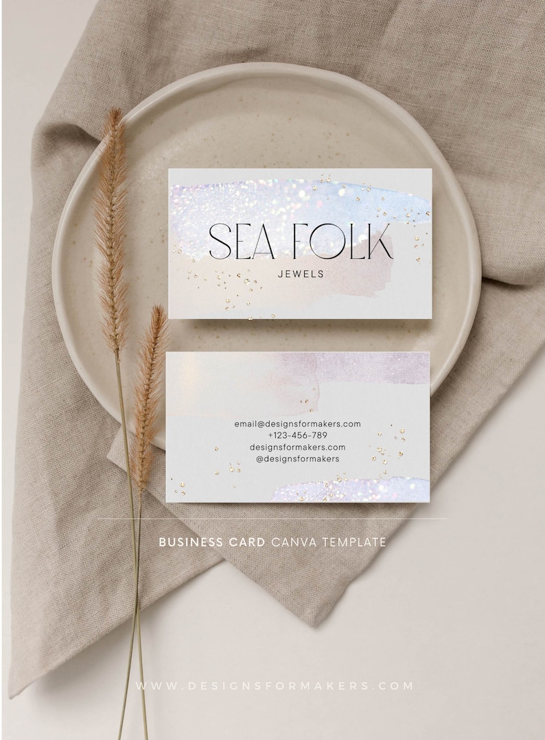 Op de afbeelding: Een visitekaartje sjabloon voor een juweliersbedrijf genaamd "Sea Folk Jewels". De kaart heeft een aquarel achtergrond in lichtblauw en roze met gouden glitter accenten. De naam van het bedrijf en de website zijn op de kaart gedrukt.