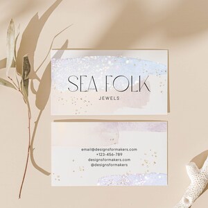Op de afbeelding: Een visitekaartje met een aquarel achtergrond in tinten blauw en roze met gouden glitter. De tekst "SEA FOLK JEWELS" staat in zwart lettertype. De kaart bevat ook contactgegevens: email@designsformakers.com, +123-456-789, designsformakers.com, @designsformakers en www.designsformakers.com.