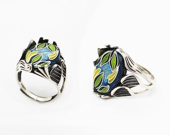 May include: A silver ring with a blue, green, and yellow enamel design. The ring is set with a large oval-shaped stone.