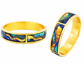 May include: A gold-toned hinged bangle bracelet featuring rectangular enamel inlays. The enamel displays a vibrant pattern of swirling blue, turquoise, and yellow waves with small white dots, set within a polished gold metal frame.