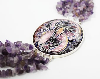 Pode incluir: Um colar com um grande pendente oval apresentando um design de esmalte em tons de roxo escuro, rosa e branco com padrões de folhas em espiral. O pendente é emoldurado em prata e ligado a vários fios de contas irregulares de ametista roxa.