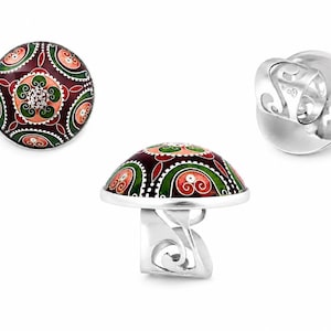 Puede incluir: Un anillo de plata con una parte superior abovedada esmaltada con un diseño floral en rojo, verde y melocotón. El anillo se muestra desde múltiples ángulos, mostrando los intrincados detalles del diseño.