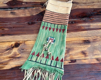 May include: A green and tan leather bag with fringe, painted with geometric designs and red accents. The bag has a strap and a beaded circle with bells attached.