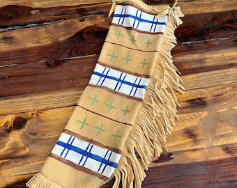 May include: A tan leather bag with fringe, decorated with blue and white stripes and green crosses. The bag has a long strap for carrying.