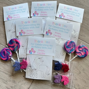 Op de afbeelding: Een set unicorn-thema feestfavorieten in doorzichtige plastic zakjes. Elk zakje bevat een kleurplaat met een eenhoorn, een lolly en drie eenhoornvormige kleurpotloden. De zakjes zijn vastgebonden met een roze lint en hebben een bedankkaartje met de tekst "Bedankt voor het vieren van mijn verjaardag met mij! Van Cecilia."