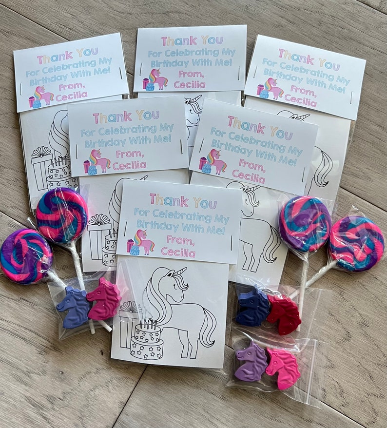 Op de afbeelding: Een set unicorn-thema feestfavorieten in doorzichtige plastic zakjes. Elk zakje bevat een kleurplaat met een eenhoorn, een lolly en drie eenhoornvormige kleurpotloden. De zakjes zijn vastgebonden met een roze lint en hebben een bedankkaartje met de tekst "Bedankt voor het vieren van mijn verjaardag met mij! Van Cecilia."