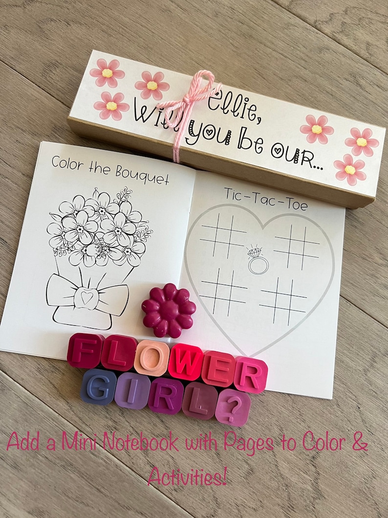 May include: A craft kit for a flower girl with a brown box, a small notebook, crayons, and a tic-tac-toe game. The box has pink flowers and the text "ellie, will you be our..." on it.