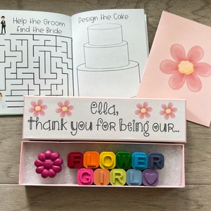 May include: A pink box with the text "Ella, thank you for being our..." and two pink flowers. The box contains a pink flower-shaped crayon and a set of rainbow crayons that spell out "FLOWER GIRL".
