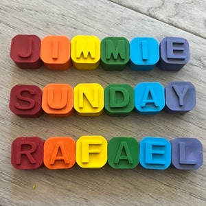 May include: A set of colourful alphabet blocks spelling out the names "Jimmie", "Sunday", and "Rafael". The blocks are arranged in a rainbow pattern, with red, orange, yellow, green, blue, and purple blocks.
