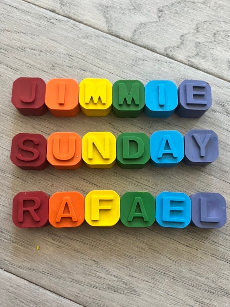 May include: A set of colourful alphabet blocks spelling out the names "Jimmie", "Sunday", and "Rafael". The blocks are arranged in a rainbow pattern, with red, orange, yellow, green, blue, and purple blocks.