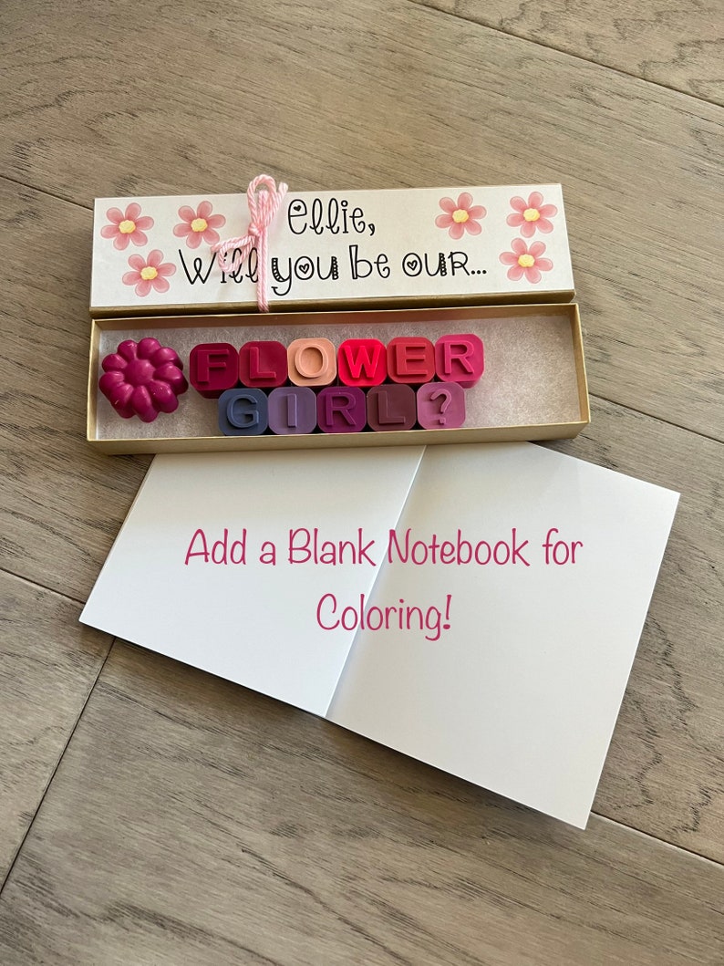 May include: A white box with pink flowers and the text "Ellie, Will you be our... FLOWER GIRL?"  The box contains colorful wax letters spelling out the words "FLOWER GIRL".