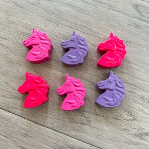 Op de afbeelding: Zes eendhoornvormige kleurpotloden in roze, paars en rood. De kleurpotloden zijn gerangschikt in twee rijen van drie.