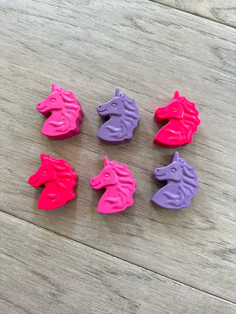 Op de afbeelding: Zes eendhoornvormige kleurpotloden in roze, paars en rood. De kleurpotloden zijn gerangschikt in twee rijen van drie.