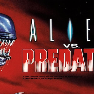 May include: An arcade game banner for Alien vs. Predator. The image features the Alien and Predator characters facing each other, with the game's title in bold, red letters. The background is a gradient of red and blue.