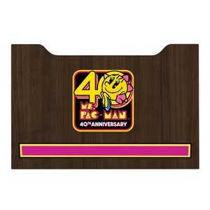 May include: A brown wooden plaque with a yellow and pink Ms. Pac-Man 40th Anniversary logo. The logo features Ms. Pac-Man with a pink bow and the text "Ms. Pac-Man 40th Anniversary".