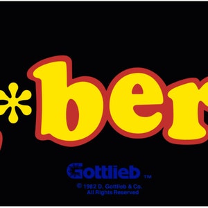 Peut inclure: Illustration de l'arcade Q*bert avec un personnage de dessin animé portant une boule violette sur la tête, un serpent et une créature verte. Le texte "Q*bert" est en jaune avec des contours rouges. Le texte "Gottlieb" est en blanc avec un contour noir.