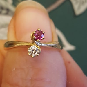 以下が含まれることがあります： ピンクと白の宝石がセットされた金の指輪。指輪は人の指にはめられています。