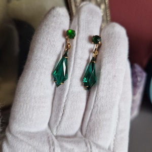 Può includere: Un paio di orecchini pendenti vintage verde smeraldo. Ogni orecchino presenta una piccola pietra verde rotonda e una pietra verde più grande a forma di goccia sfaccettata. Il metallo è dorato.