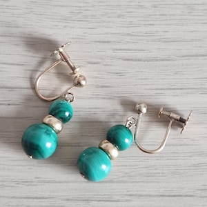 May include: A pair of screw-back earrings featuring two round malachite beads in varying sizes separated by a small silver-toned metal spacer bead. The earrings have a polished finish and a distinct green banded pattern on the natural stone beads.