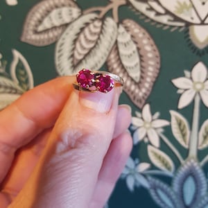 Może przedstawiać: Złoty pierścionek z dwoma czerwonymi kamieniami szlachetnymi osadzonymi w skręconej obrączce.