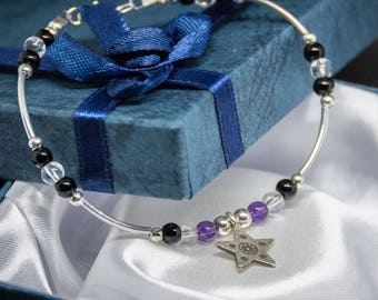 May include: A silver bracelet with black, white, and purple beads and a silver star charm. The bracelet is in a blue gift box with white satin lining.