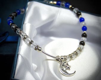May include: A silver bracelet with a crescent moon and star charm. The bracelet is made with clear, black, and blue beads.