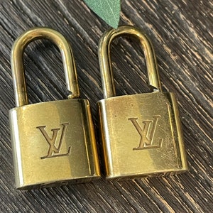 Puede incluir: Dos candados de color dorado con el logotipo de Louis Vuitton grabado en la parte delantera.